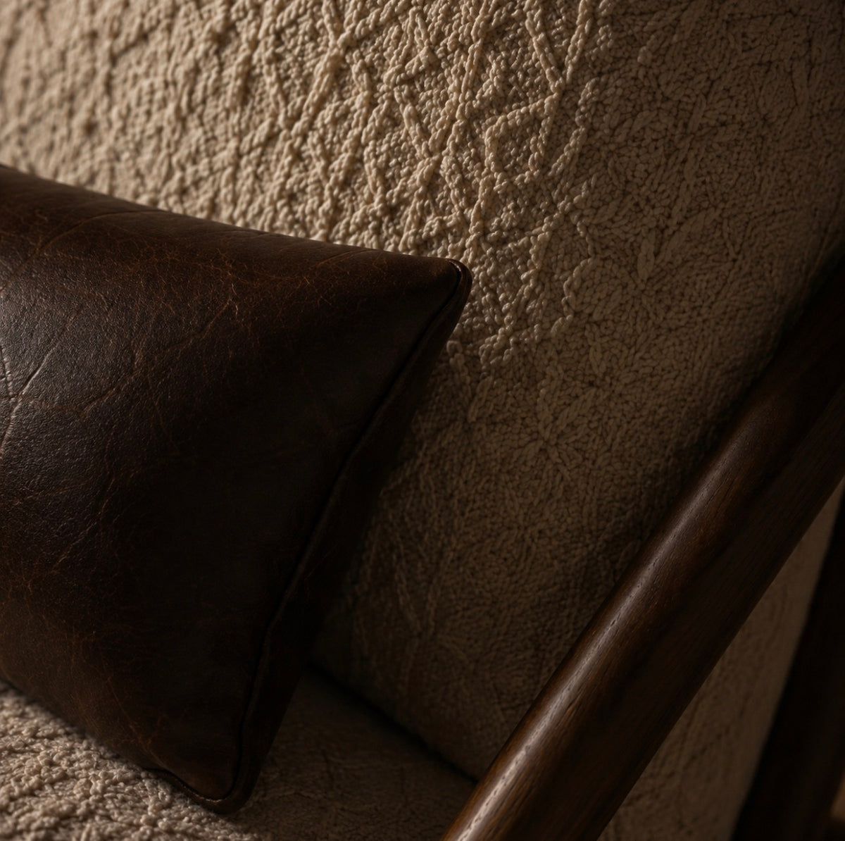 Close detail of the brown leather lumbar cushion against the textured bouclé upholstery